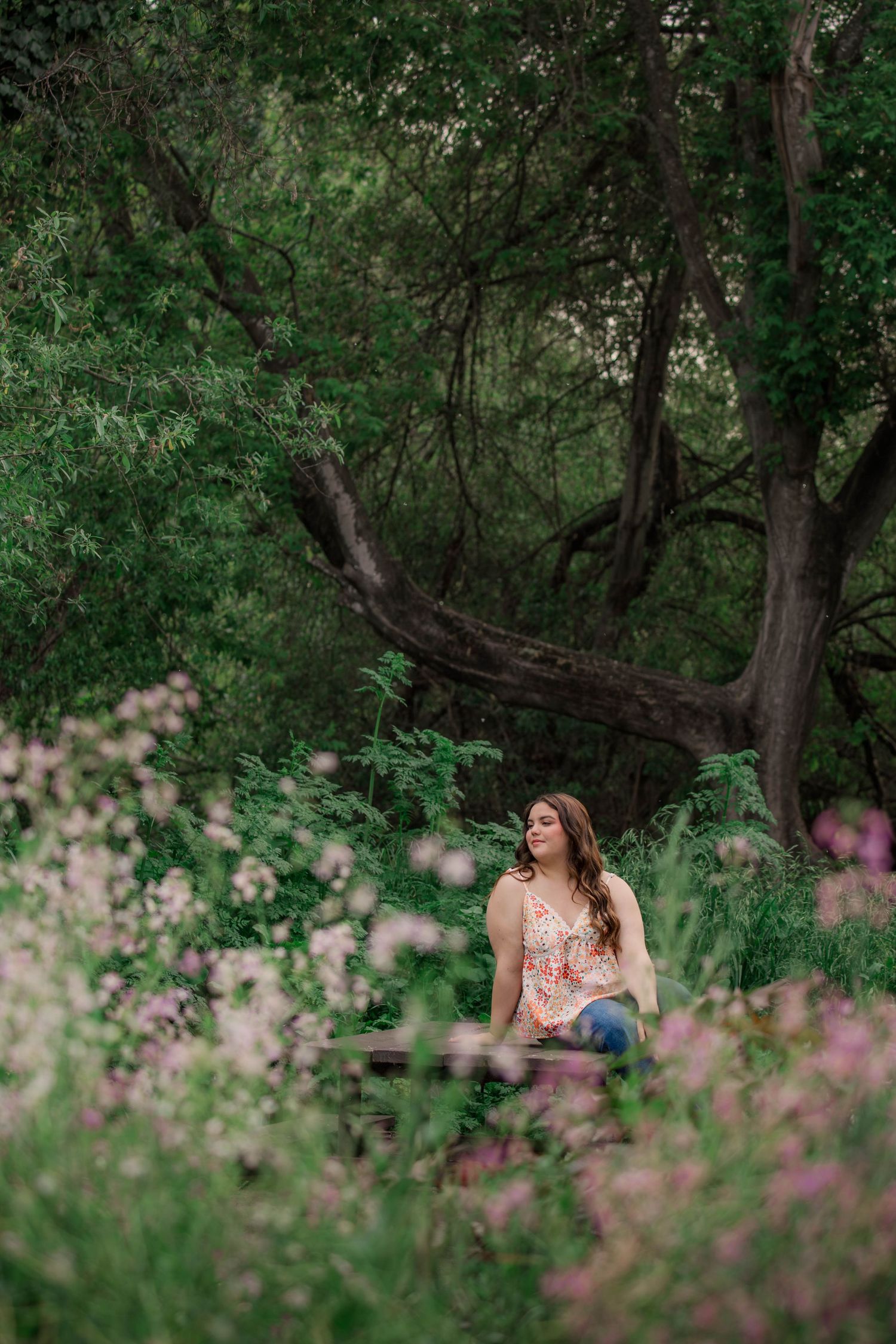 A tranquil forest scene with pink wildflowers in the foreground and lush green trees creating a natural backdrop.