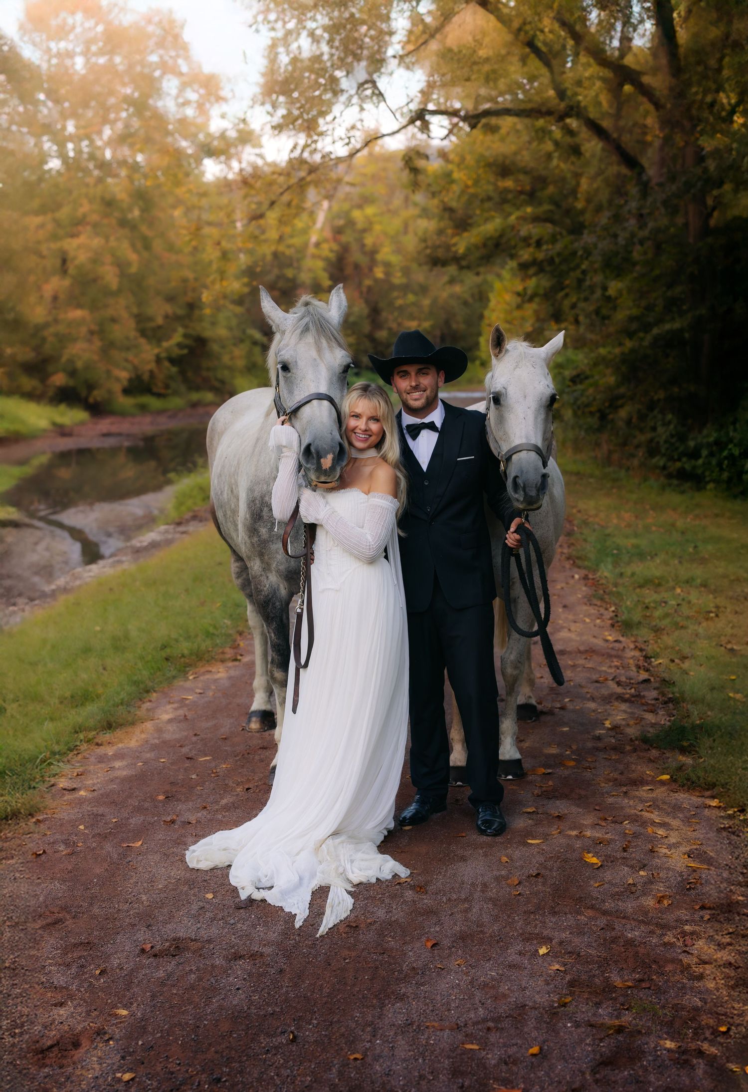 A romantic wedding photo series showing a couple with two white horses on a rustic autumn path in the woods.
