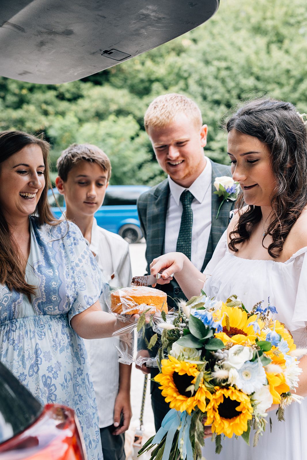 Wedding party smiling and laughing together while holding bright yellow sunflower bouquets outdoors.