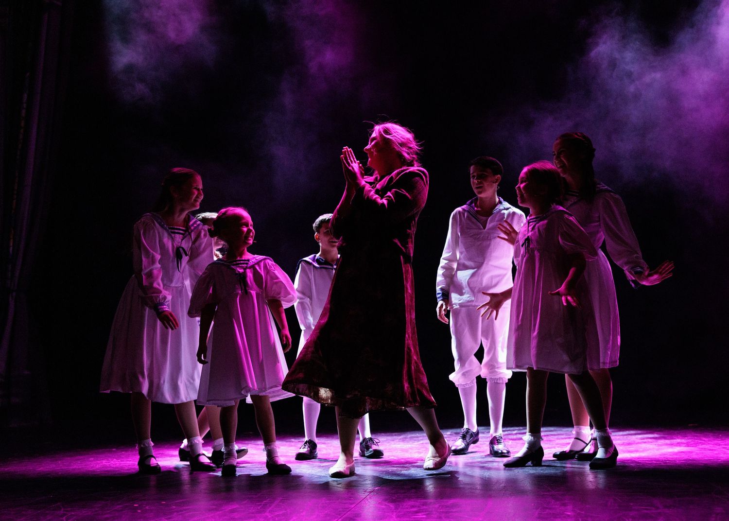 Dancers perform on stage under dramatic purple lighting in a contemporary dance piece.