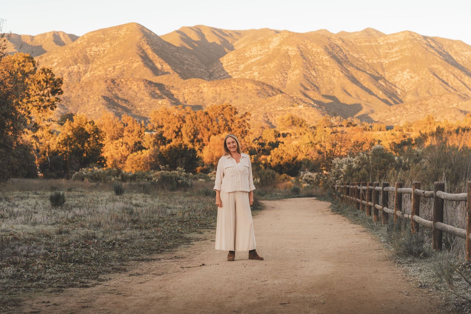 A couple stands on a desert trail at sunset with golden mountains in the background.