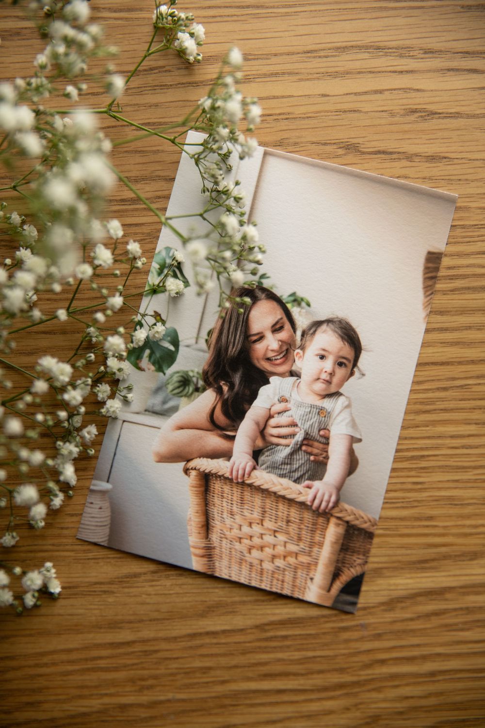 A photograph of a family portrait lies on a wooden surface with delicate baby's breath flowers scattered around it.