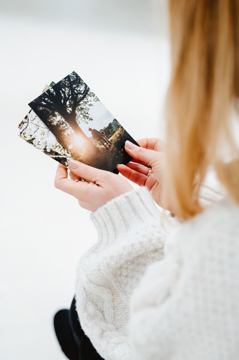 Hands holding printed photographs against a white sweater background with soft natural lighting and warm tones.