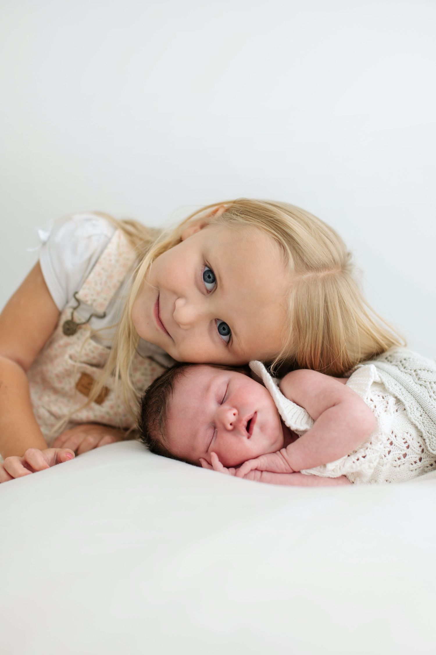 A tender moment captured in white as a young child and baby lay close together on soft bedding.