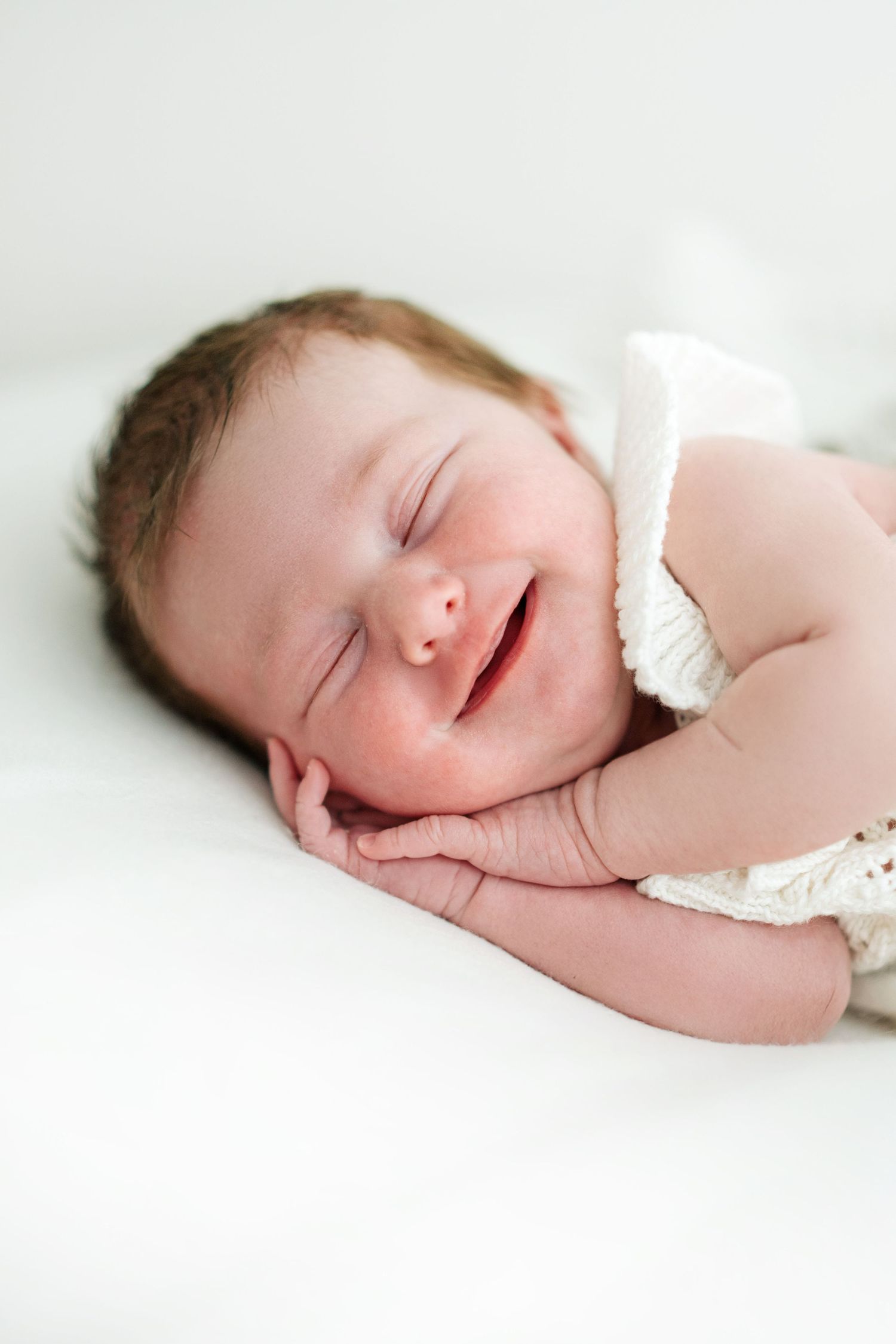 A peaceful sleeping newborn baby wrapped in soft white fabric against a light background.