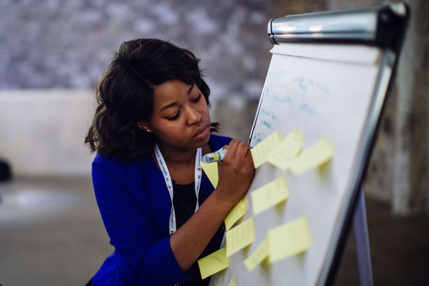 Professional writing on sticky notes on a flip chart board while wearing a blue blazer.