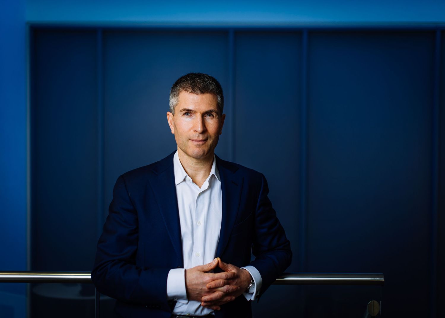 Professional portrait against a dark blue background in business attire.