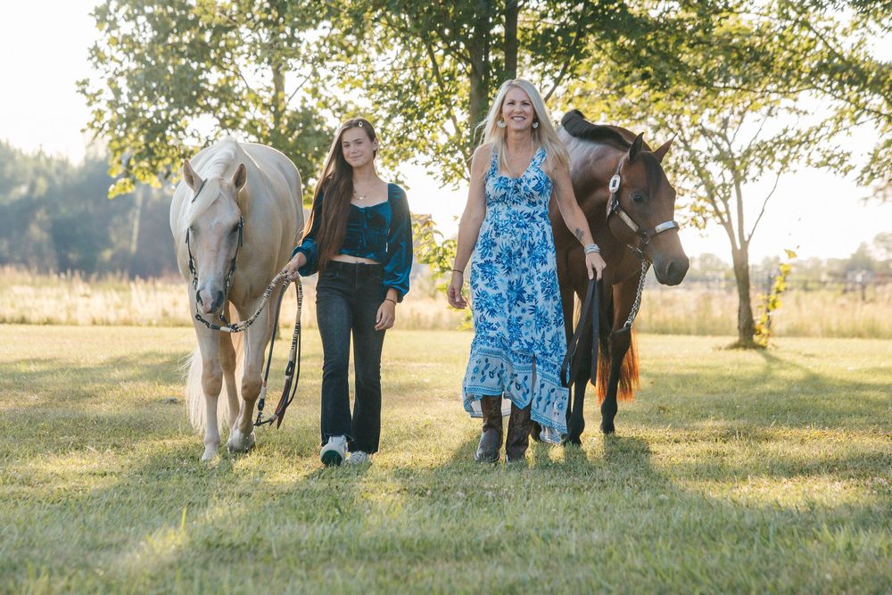 A family stands with horses in a sunlit field during golden hour, creating a warm and peaceful outdoor scene.