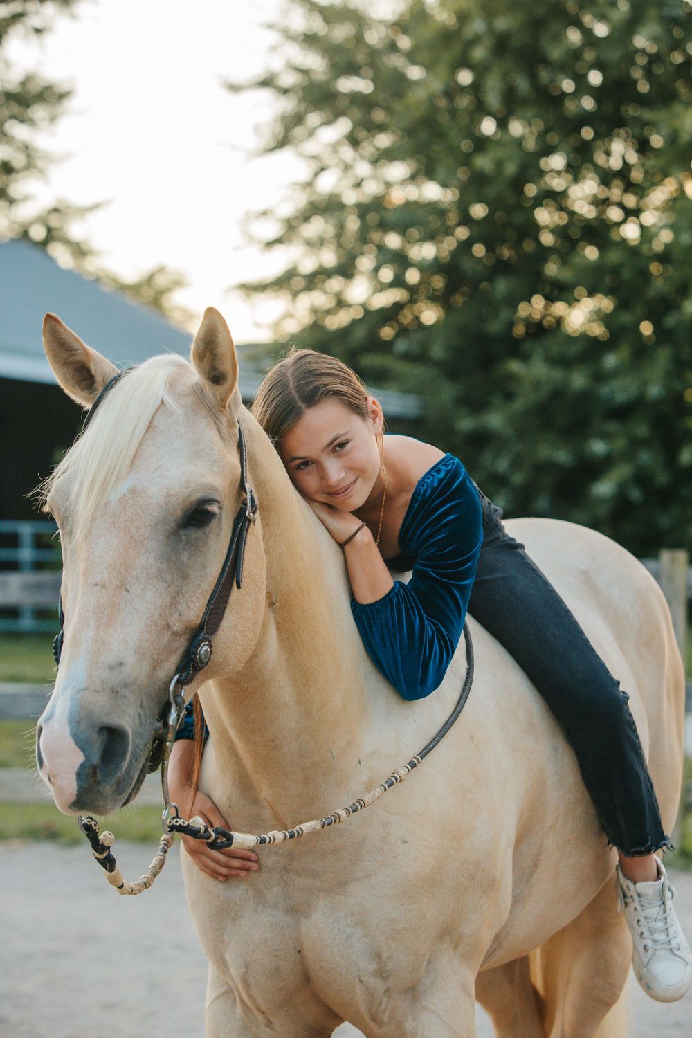 A white horse and rider share a tender moment outdoors during a golden sunset in a tranquil setting.