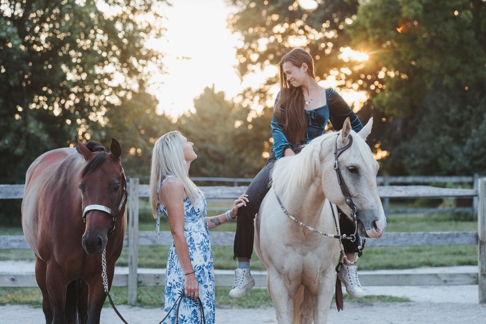 A group of riders lead their horses along a scenic path during golden hour with white fencing in the background.