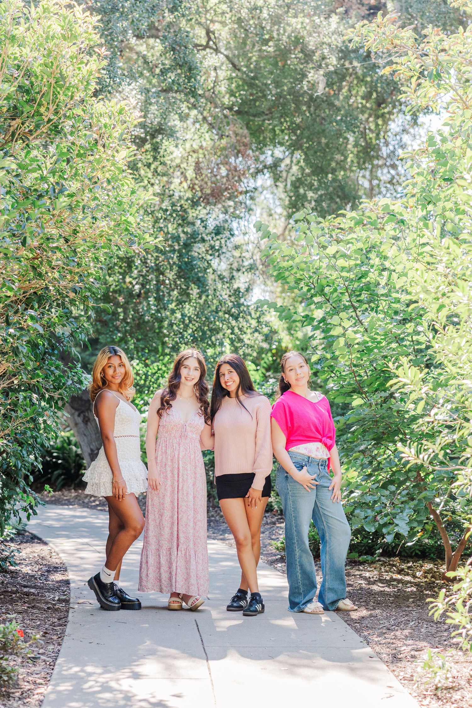 A group of friends pose playfully in a garden setting showing off their outfits and shoes.