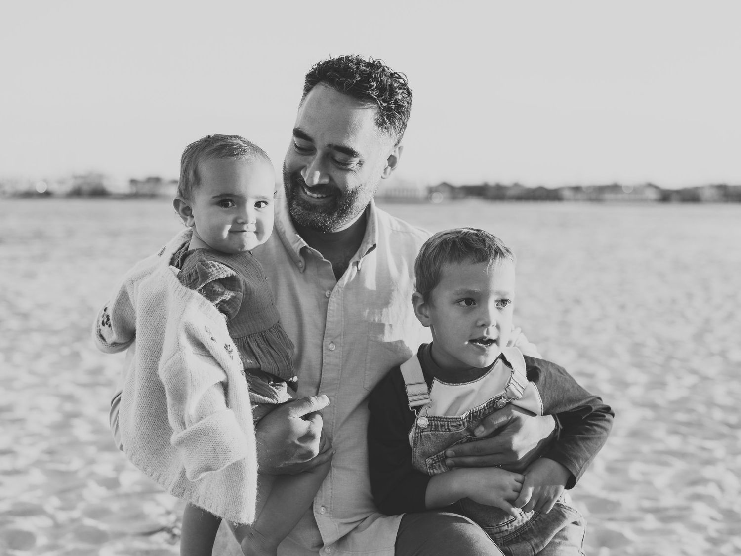 Close-up of father holding his two children with waves in the background.