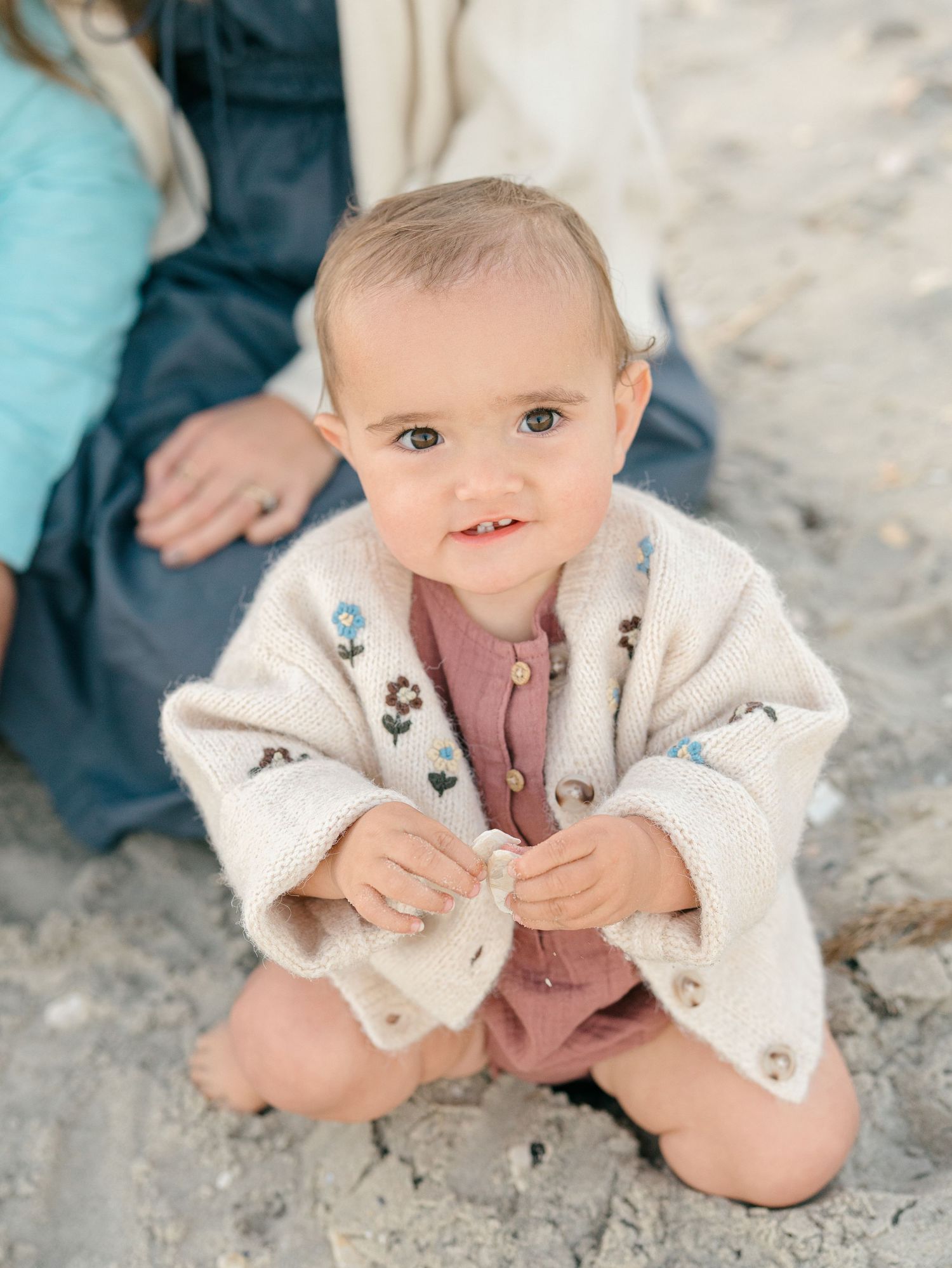 Close-up of little girl on the beach with a pink dress and floral tan sweater.