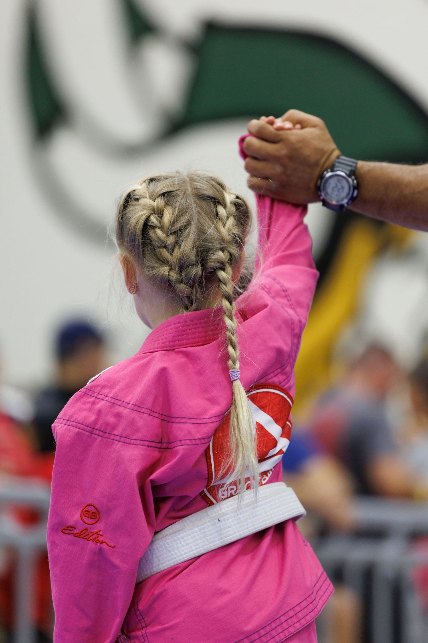 Martial artist in pink gi with braided hair competing at tournament.