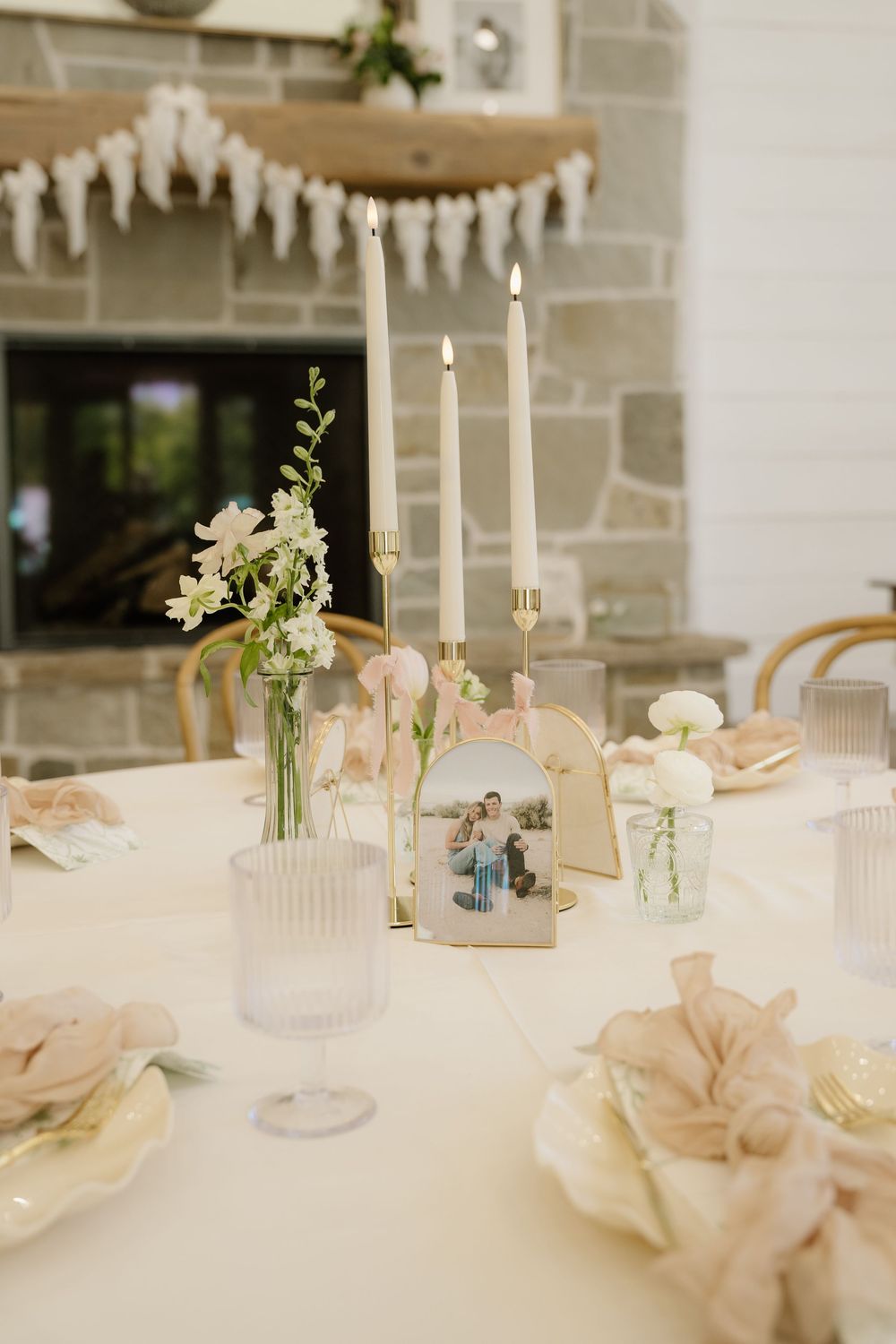 Elegant wedding table setting with white candles, roses, and delicate decor in soft neutral tones.