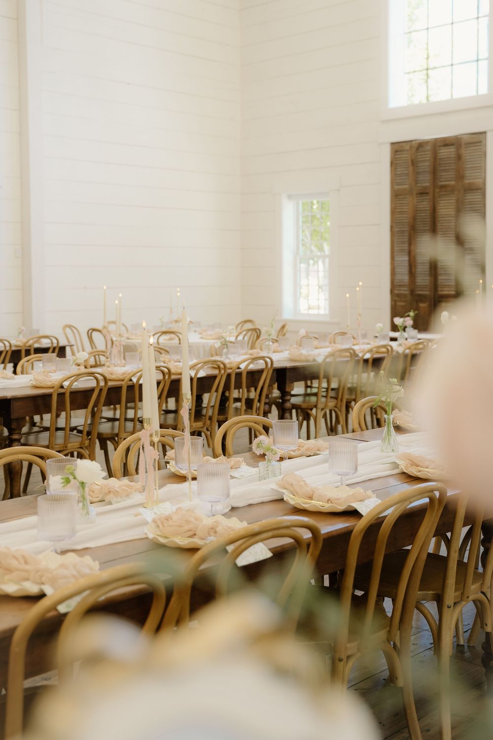 An elegant reception room with wooden chairs and white tablecloths set for a wedding celebration.