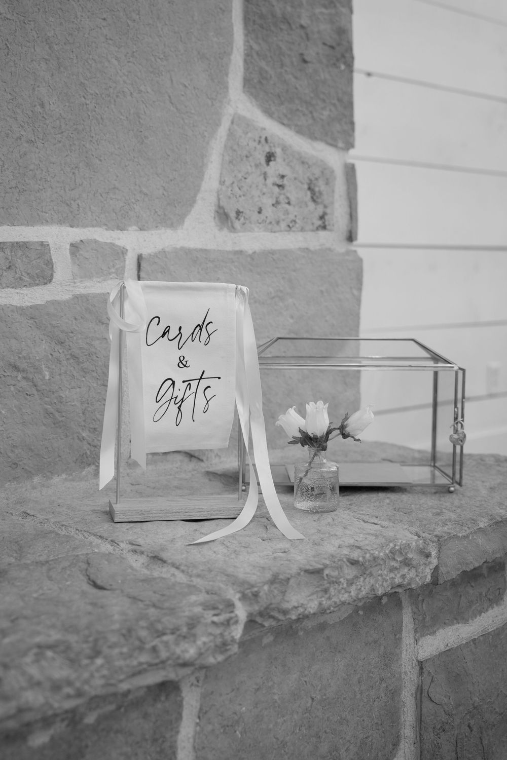 Black and white photo of cards and gifts sign with glass box decoration on stone ledge.