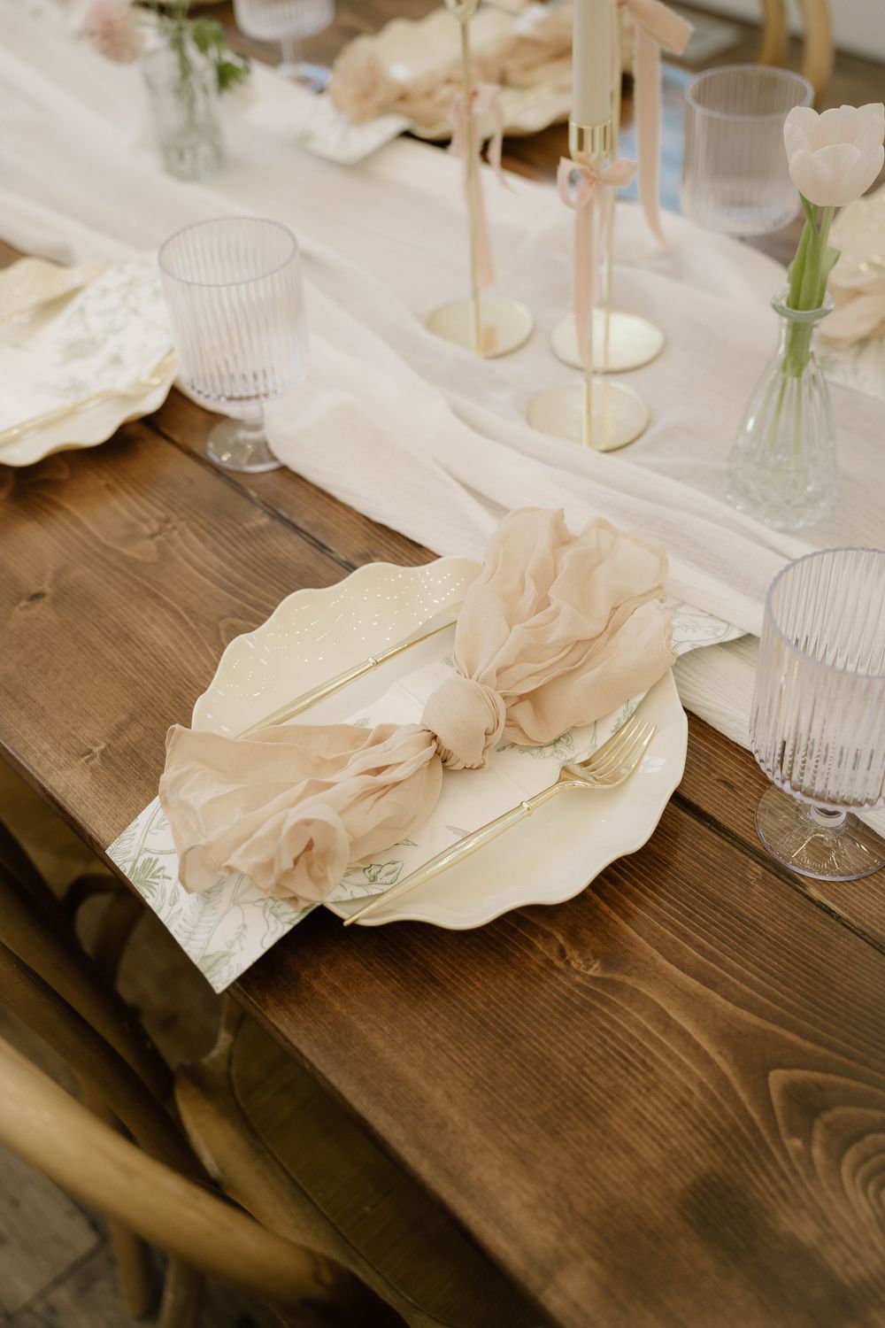 Place settings with blush napkins and glassware arranged on rustic wooden tables.