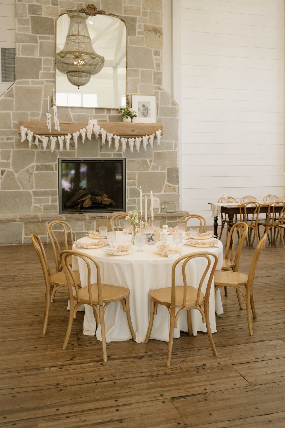Reception hall with rustic stone walls and wooden chairs arranged around white-clothed round tables.