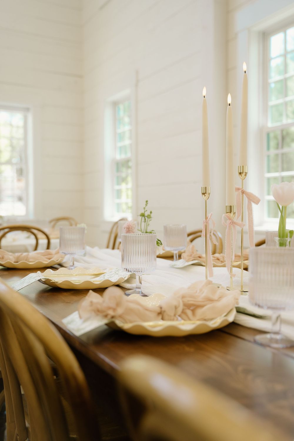 White taper candles and decorative shell-shaped dishes adorn wooden tables in a light-filled reception space.