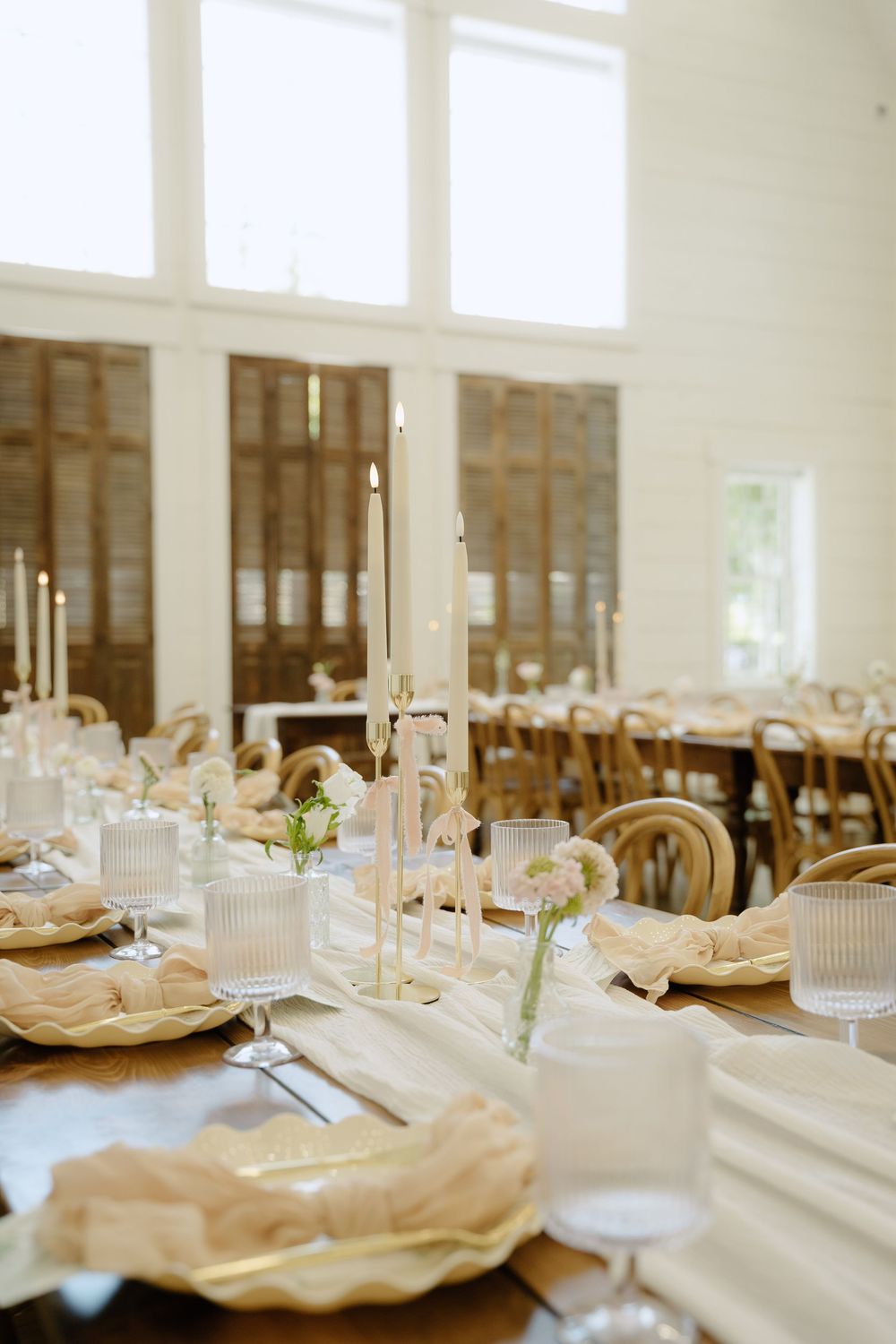 Wedding reception tables set with delicate place settings, candles, and soft floral arrangements.