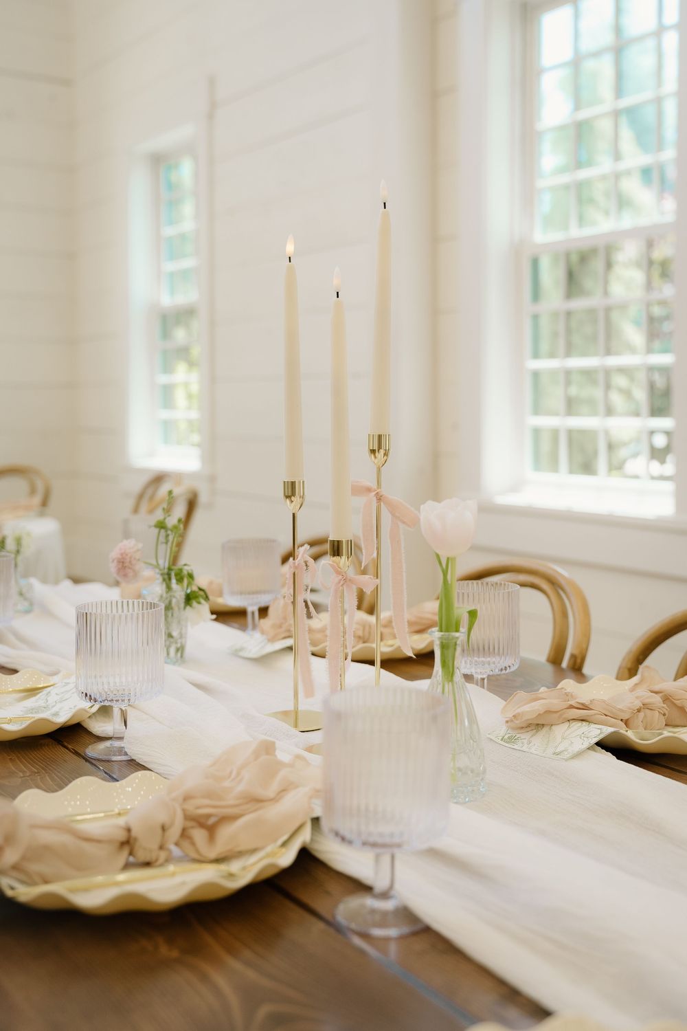 Elegant table setting with tall white candles, crystal glasses, and neutral linens for wedding reception.