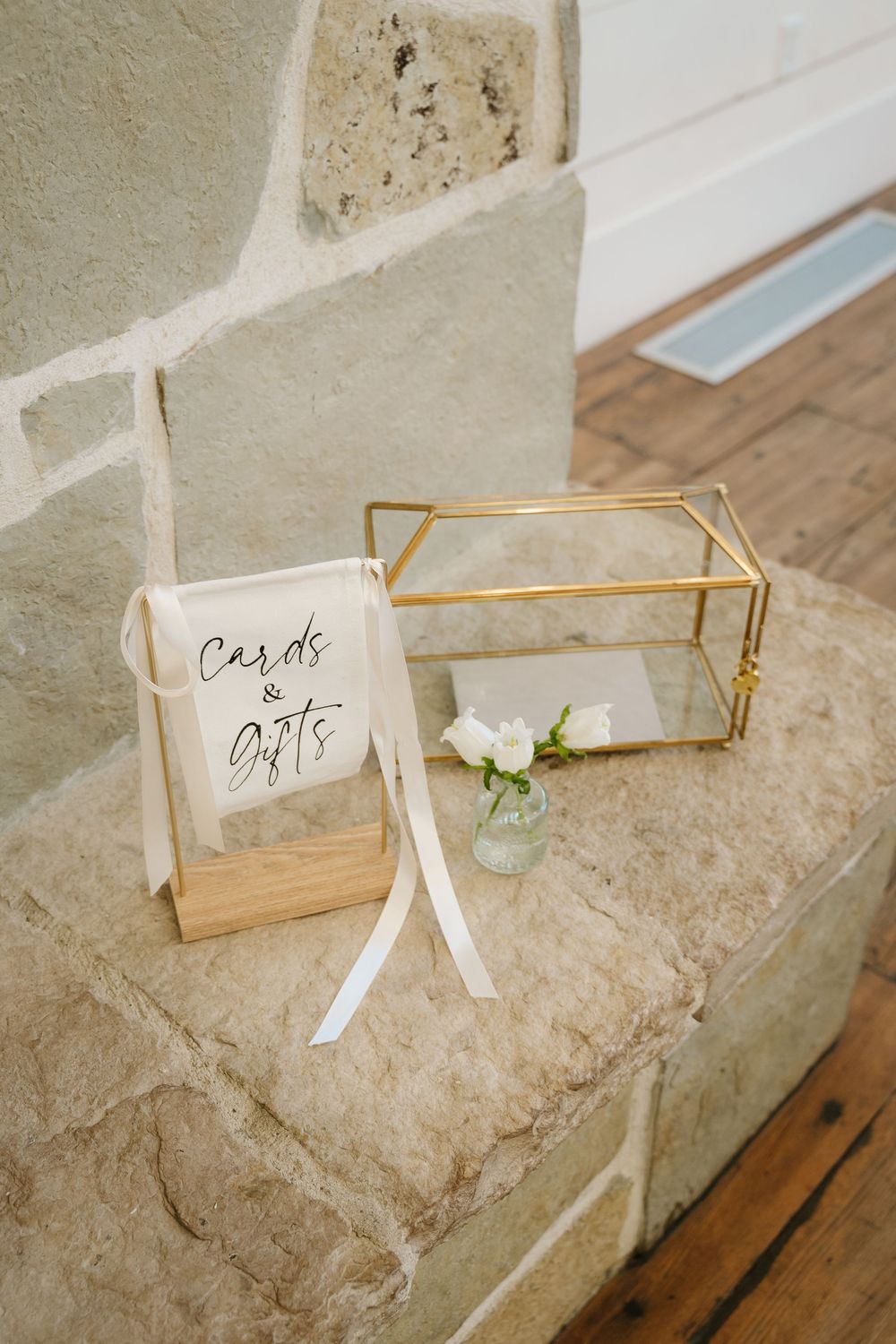 Wedding cards and gifts display with glass box and white floral accent on stone ledge.