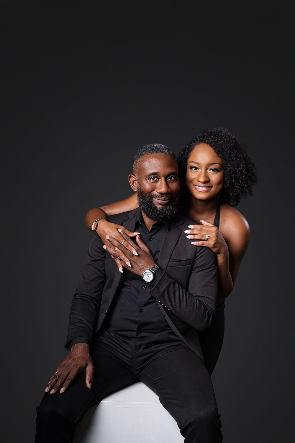 A couple in black outfits poses intimately against a dark background in a romantic photoshoot series.
