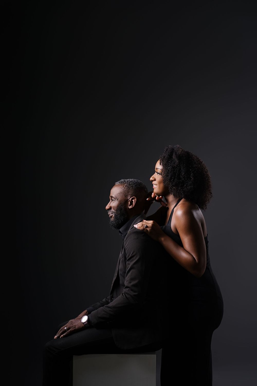 Two people in black clothing create dynamic poses against a moody dark backdrop.