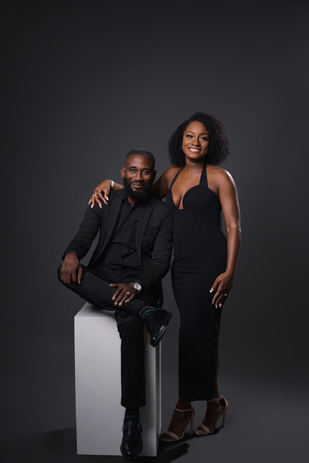 Professional studio portraits of couple in black attire posing together against dark background.