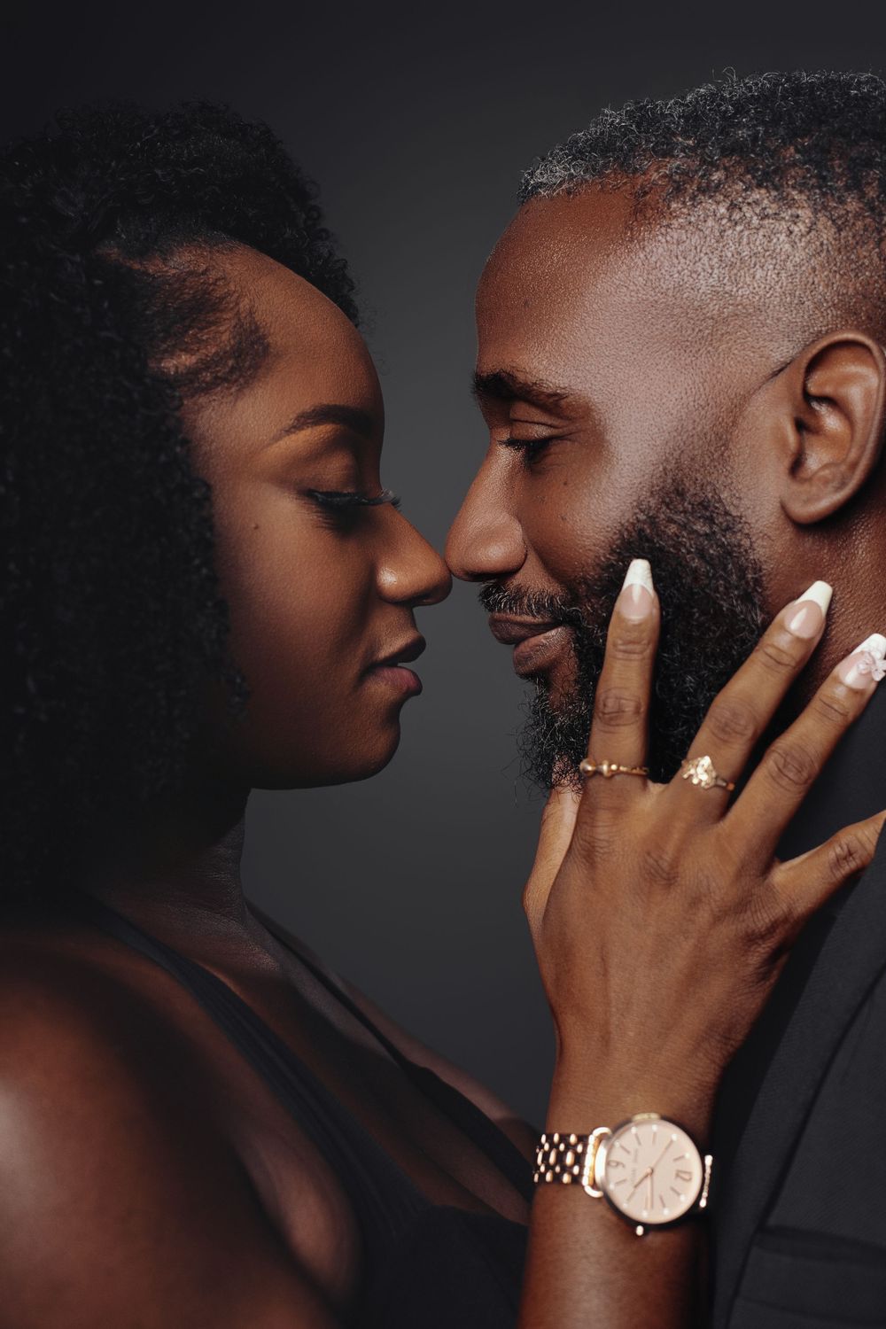 Close-up artistic portrait capturing tender moment between couple with focus on jewelry and gentle touch.