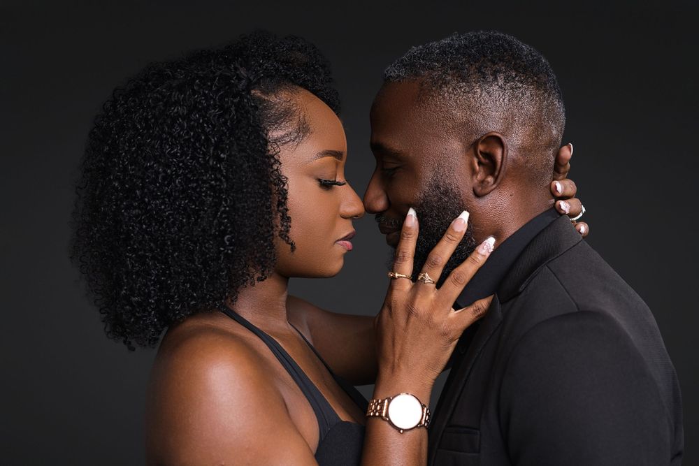 Intimate couple poses against dark background in romantic studio portrait showing tender affection.
