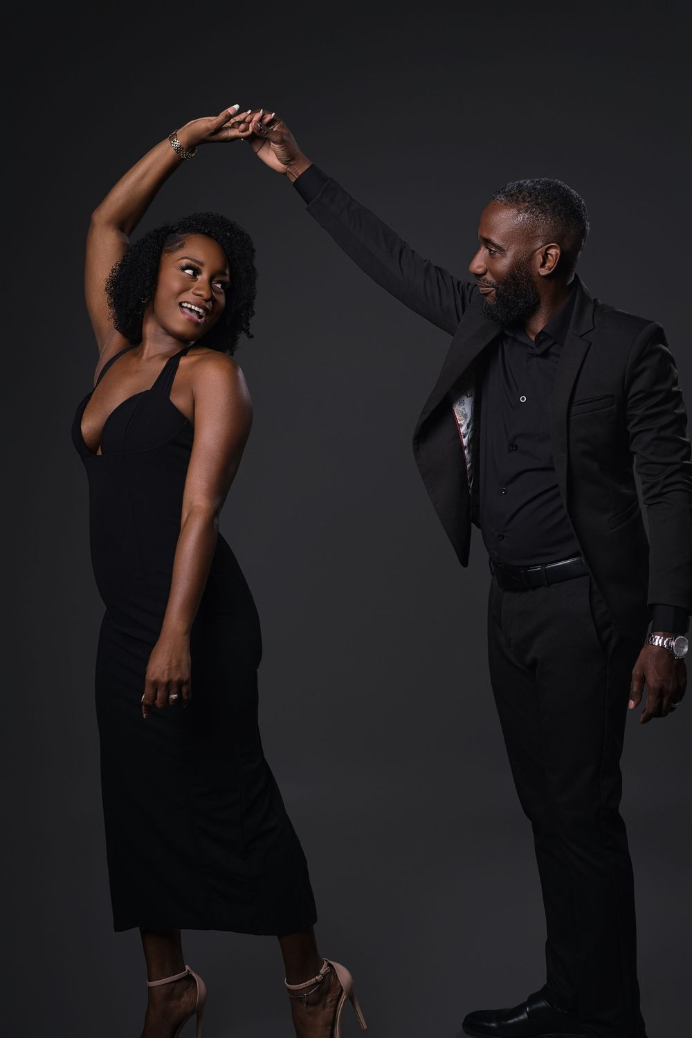 A couple dances dramatically in formal black attire against a dark studio backdrop.