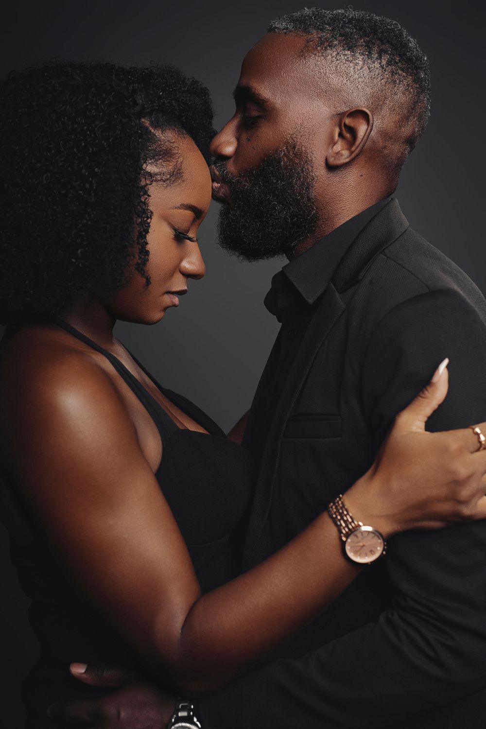 A romantic couple embraces intimately against a dark background in a series of sensual portrait photographs.