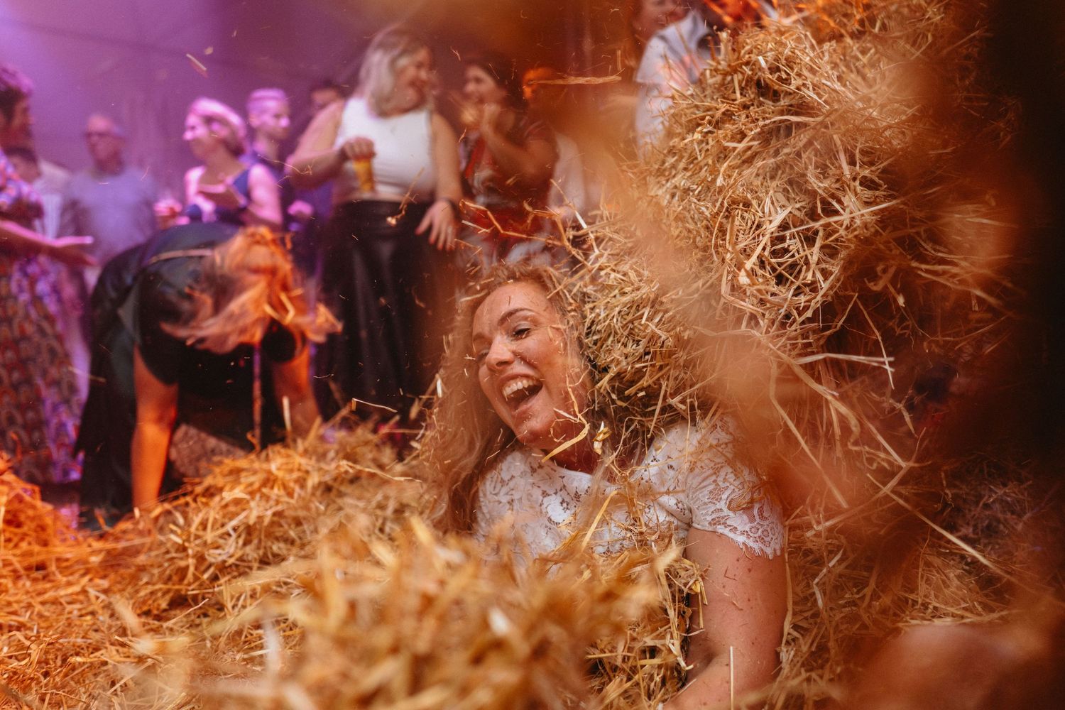 Een bruid die uitbarst van het lachen omdat ze bedolven wordt onder het stro tijdens haar avondfeest.