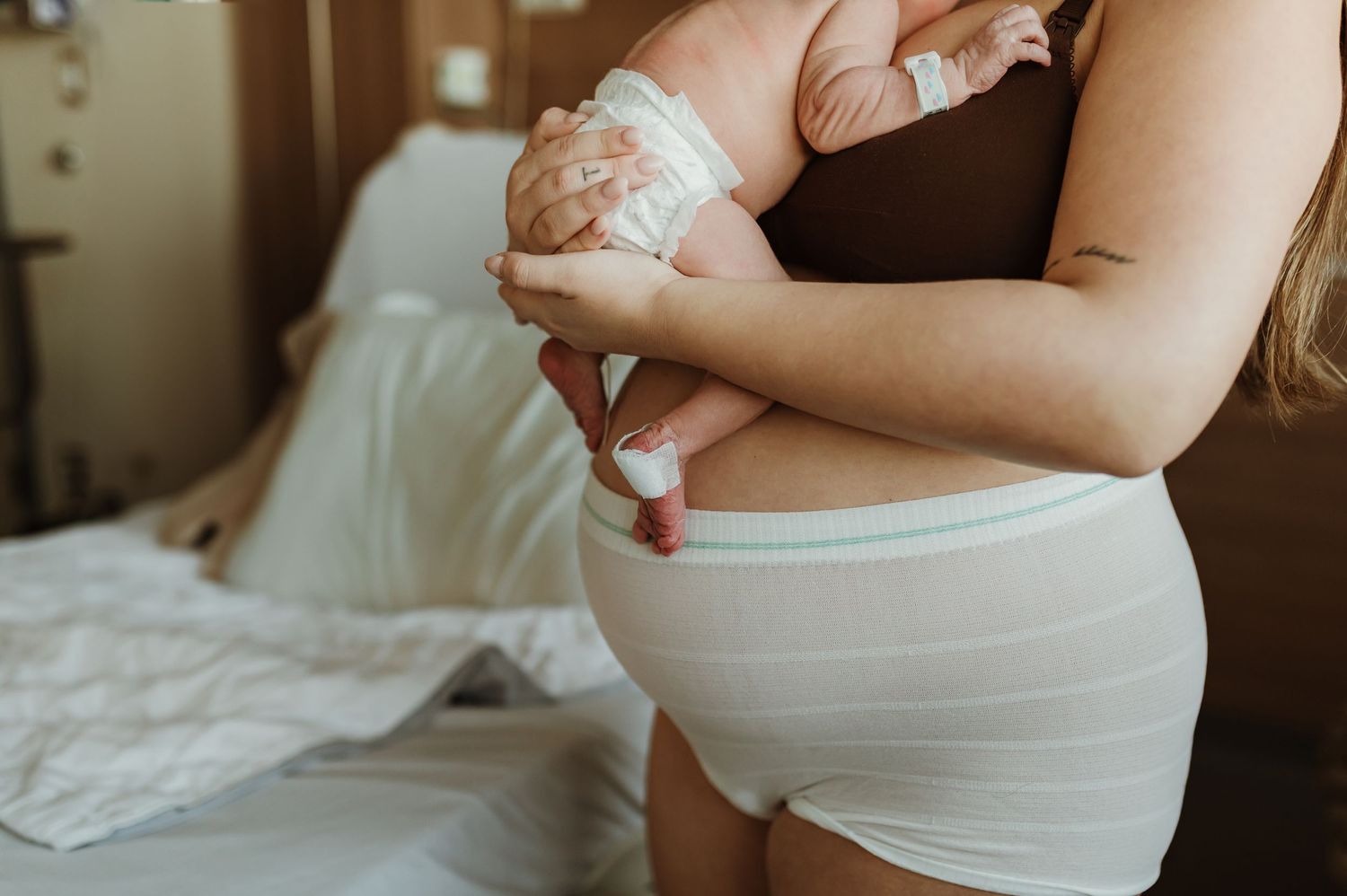 Close-up of hands gently holding a newborn baby wrapped in white swaddling cloth against a soft neutral background.