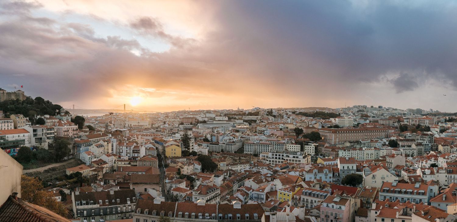 Panoramic cityscape of Lisbon Portugal at sunset with historic buildings and orange sky over the urban landscape.