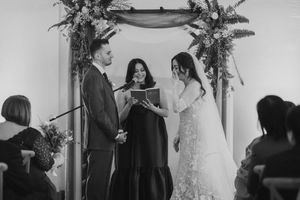 Wedding ceremony setup with floral arch and guests gathering in an elegant indoor venue.