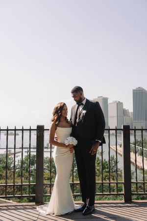 Elegant couple poses on terrace with NYC skyline backdrop during wedding photoshoot.