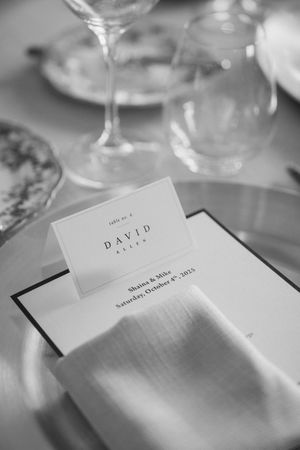 Wedding place card for David sits among wine glasses on formal dining table.