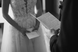 Person in white dress reads from paper in intimate black and white moment.