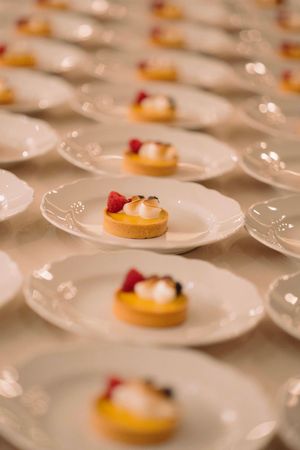 Rows of elegant white plates with delicate desserts garnished with raspberries.