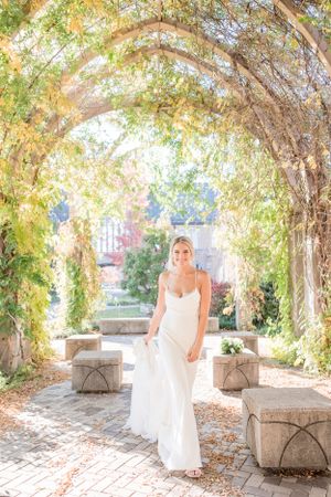 Bride in white dress walking through a garden archway covered in autumn foliage.