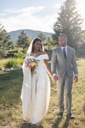 Romantic outdoor wedding photos with couple walking through sunlit mountain meadow.