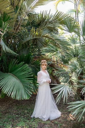 A white dress stands out against lush tropical palm fronds and greenery.