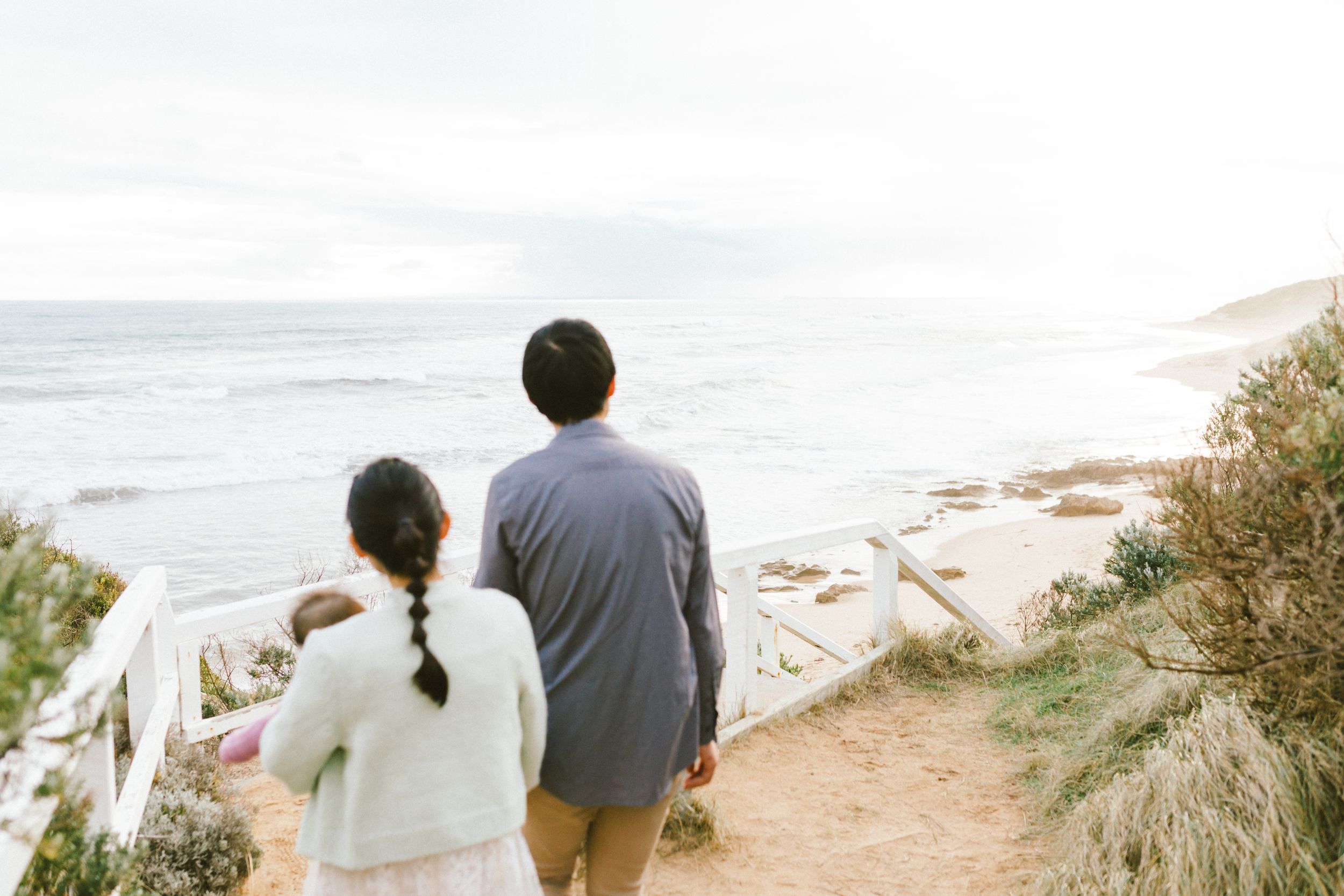 A couple stands at the edge of a coastal cliff overlooking a scenic beach and ocean view on a sunny day.