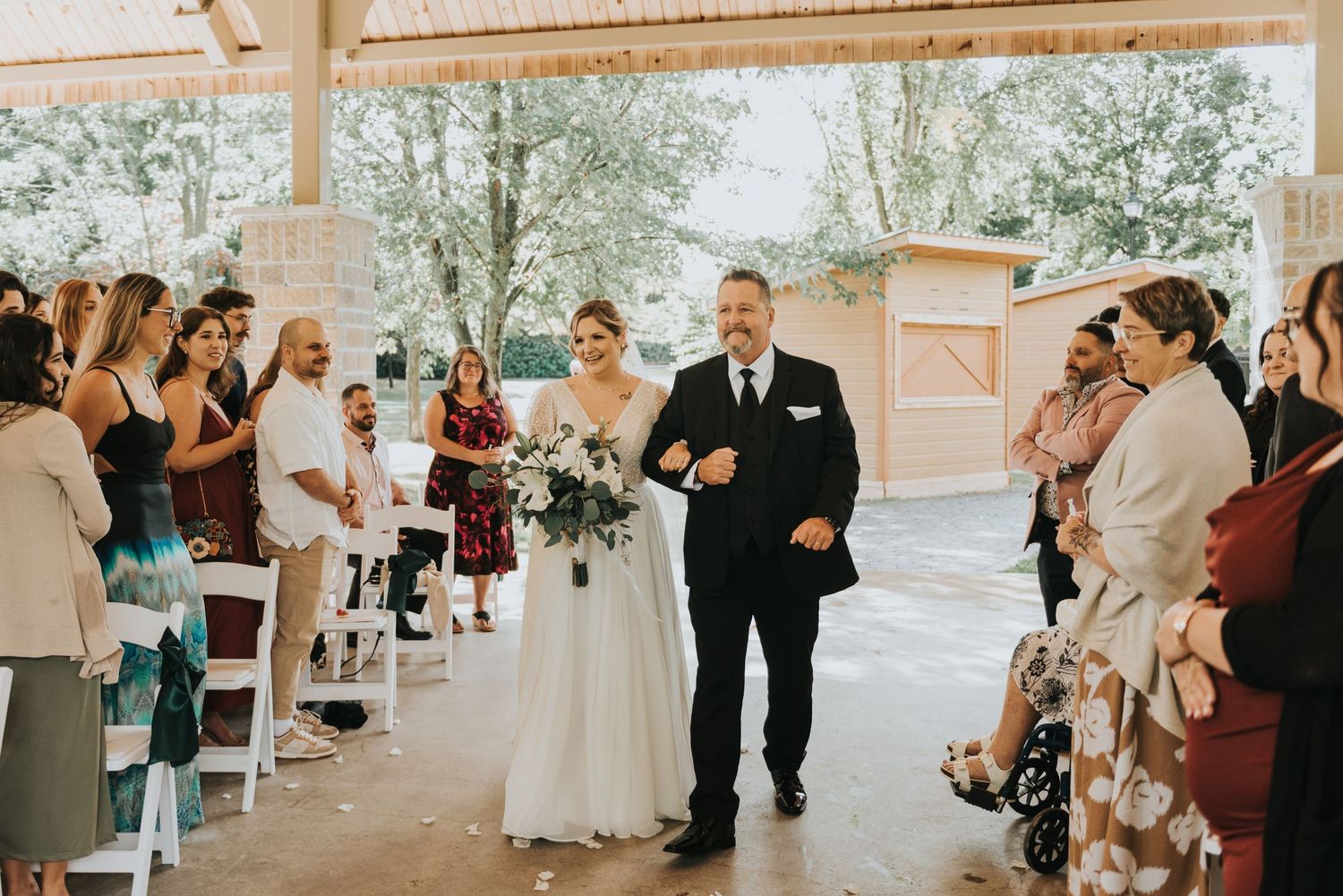Wedding guests gather outdoors at a rustic venue with string lights and wooden beams creating a romantic atmosphere.