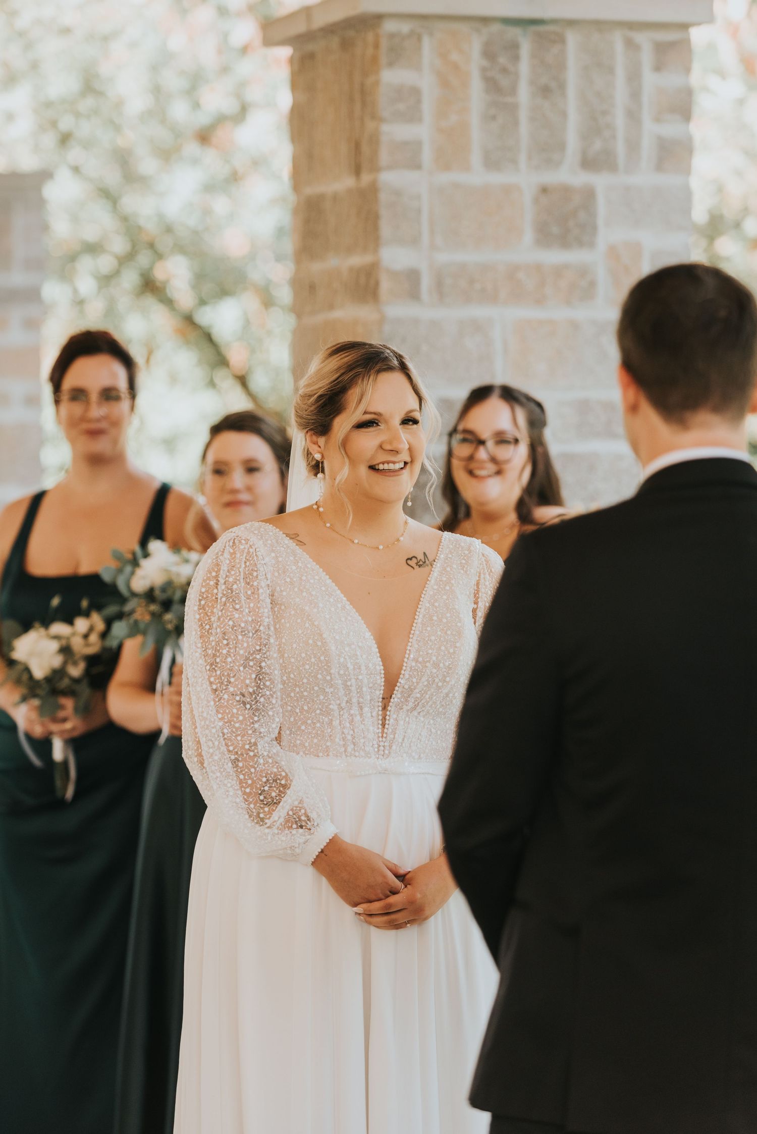 A wedding ceremony with the bride in a long-sleeved lace gown and bridesmaids in dark dresses standing at the altar.