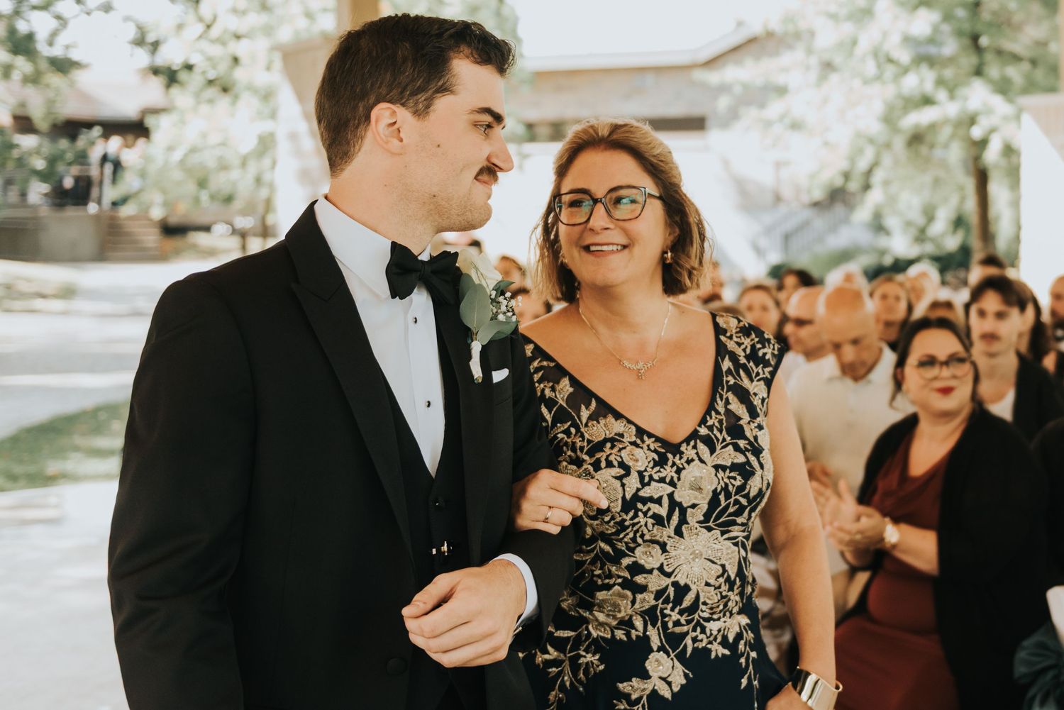 A formal event with a person in a black tuxedo walking arm in arm with someone wearing a black and white floral dress.