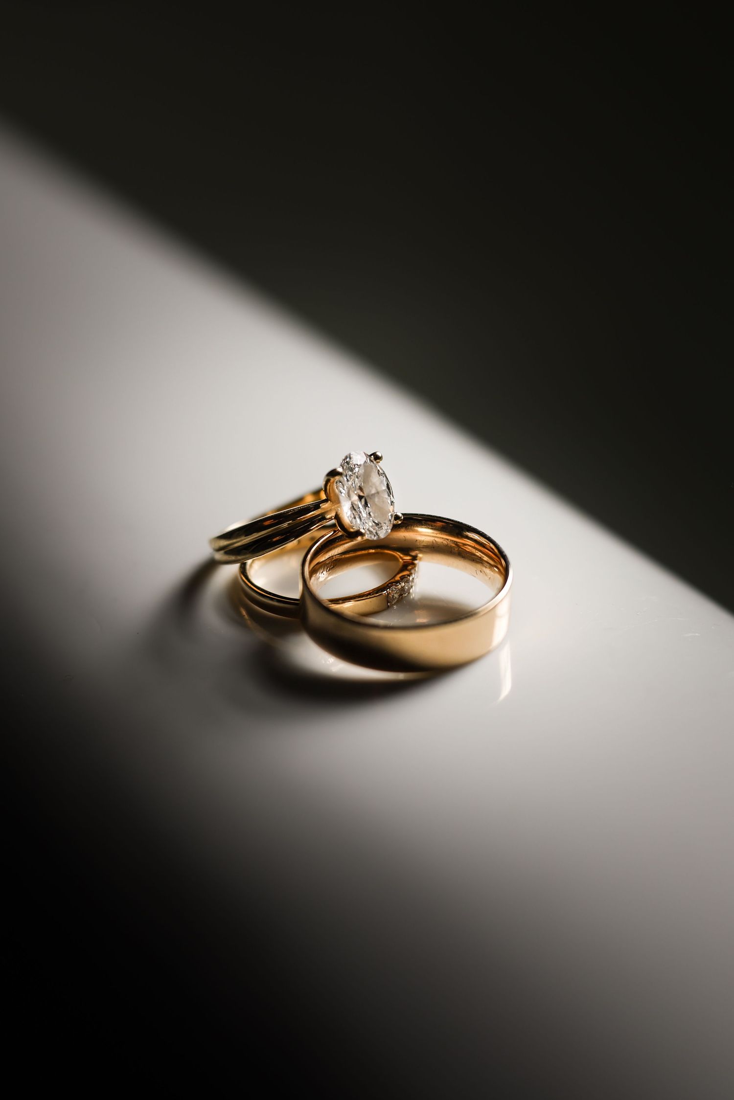 Wedding rings casting dramatic shadows on a white surface in artistic lighting.
